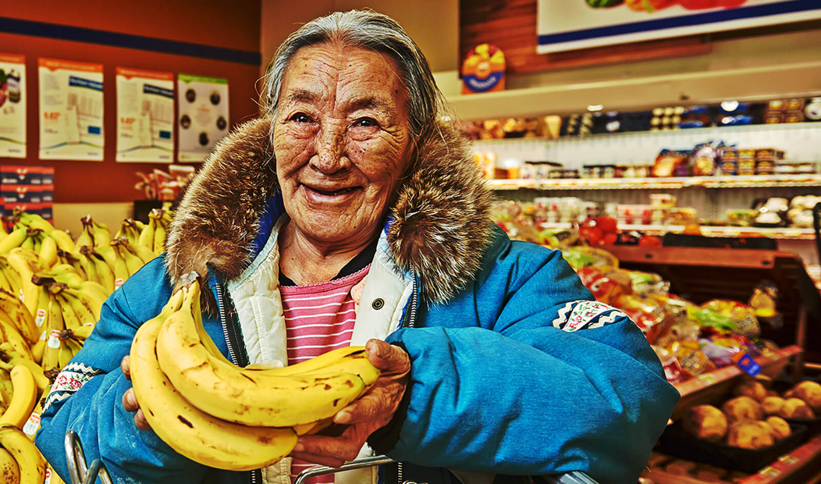 Elder wearing a blue winter parka in Arviat smiling while holding bananas