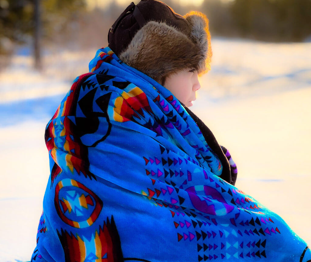a young boy wrapped in a traditional blanket with a fur hat.