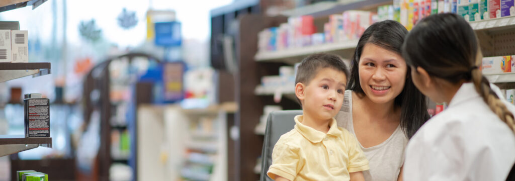 A mother holding a small child speaking with a pharmacist